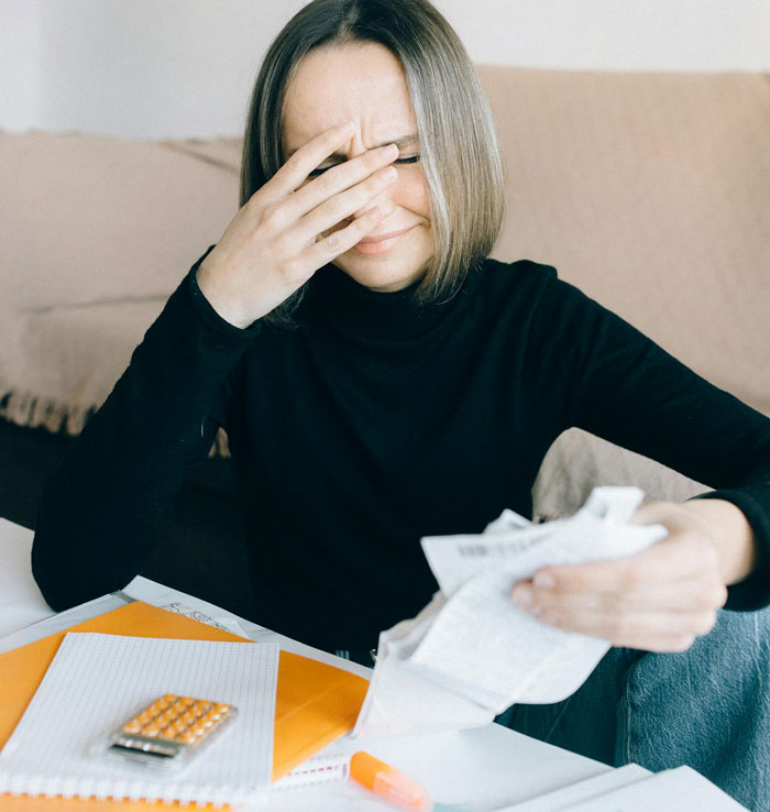 Tired woman quietly coping with stress in marriage, sitting at table with papers and medication, showing exhaustion and frustration.