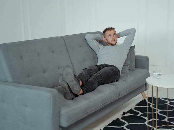 Young man looking tired and disengaged, lying on a gray couch reflecting quiet quit feelings in marriage.