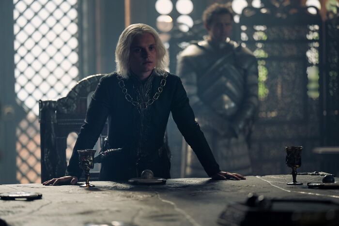 Young Aegon Targaryen, known as Egg, with platinum hair in a dimly lit throne room from the Game of Thrones universe.
