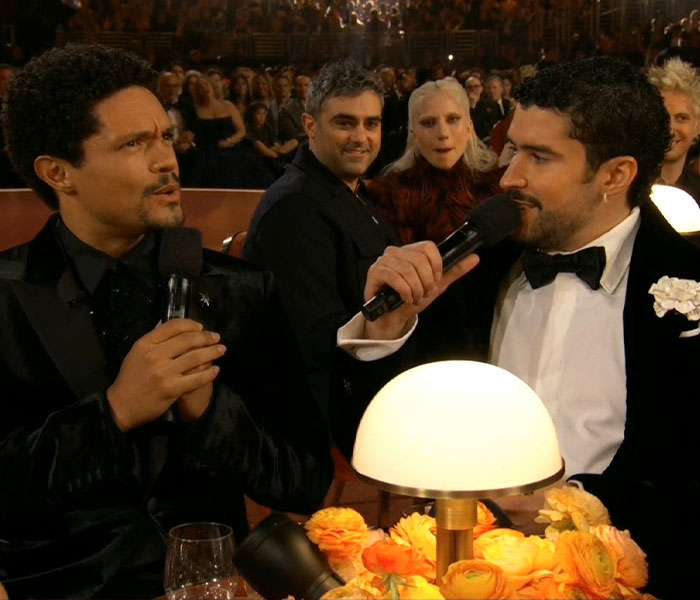 Two men in formal wear holding microphones during awkward celebrity reactions at the 2026 Grammy Awards.