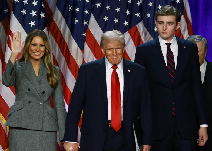 Donald Trump standing with Melania and Barron Trump in front of American flags, highlighting Barron&rsquo;s height difference.