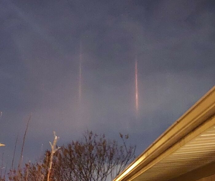Sky at dusk showing two vertical light pillars above trees and roof, illustrating strange things people witnessed that made them question.