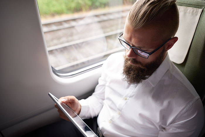 Man with glasses and beard working on a tablet inside a train, symbolizing top employee delivering record results.