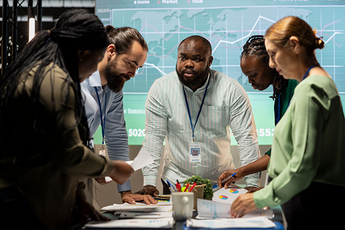 Diverse employees collaborate intensely around a table with charts and data, highlighting top employee record results.