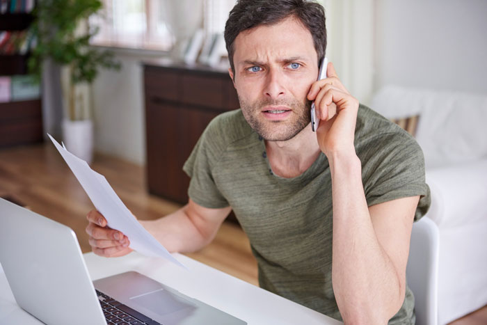 Man looking disgusted while holding a paper and talking on phone, confronting thief girlfriend about credit card use