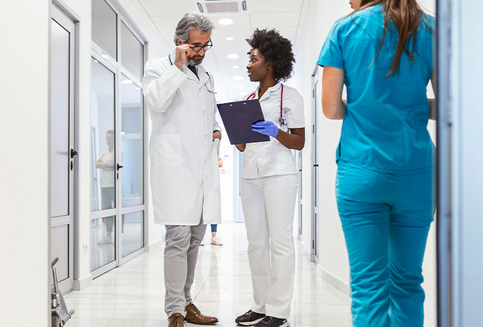 Two doctors discussing patient notes in a hospital corridor, highlighting man buys wife new bras work nickname story.