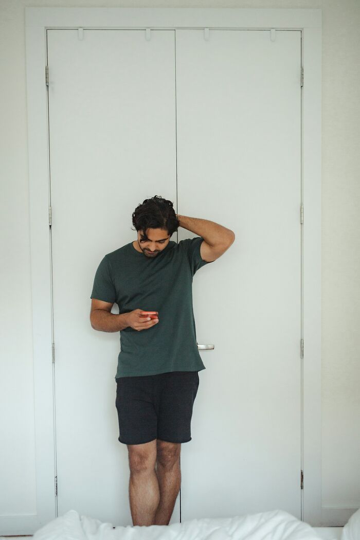 Man standing by a door looking at his phone, possibly showing signs of red flags on a first date experience.