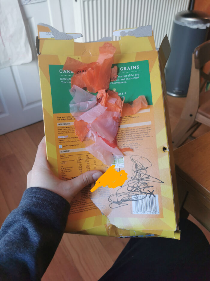 Hand holding a torn cereal box with crumpled tissue paper and scribbles, illustrating funny harmless conspiracy theories.