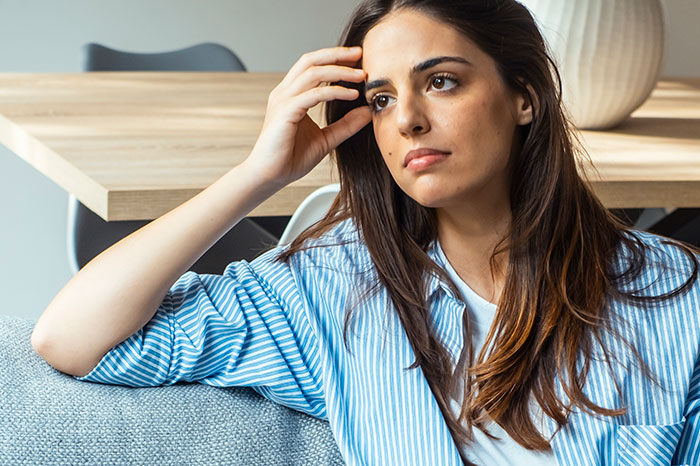 Woman in a blue striped shirt sitting thoughtfully on a couch, reflecting on how to respond to weaponized incompetence.