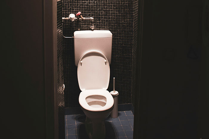 Toilet with open lid in a dark tiled restroom, illustrating concepts of incompetence and responding effectively.