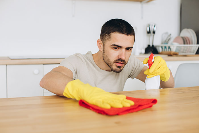 Man wearing yellow gloves focused on cleaning a wooden surface, illustrating responses to weaponized incompetence.