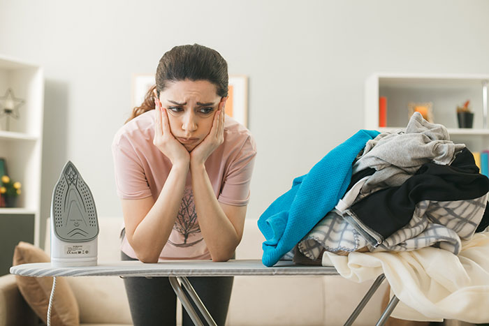 Stressed woman leaning on ironing board with pile of clothes, illustrating responses to weaponized incompetence.