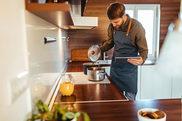 Man in apron cooking on stove while holding tablet, illustrating ways to respond to weaponized incompetence.