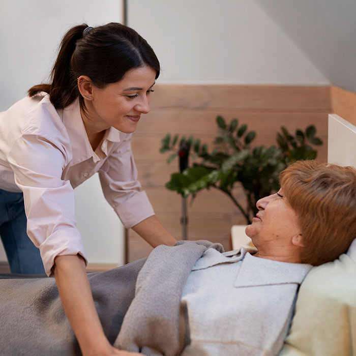 Young woman caring for an elderly woman in bed, showing compassion and support in a cozy home setting.