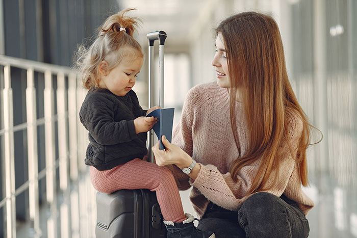 Mother and toddler daughter at airport with suitcase and passports illustrating reasons people give to have kids.
