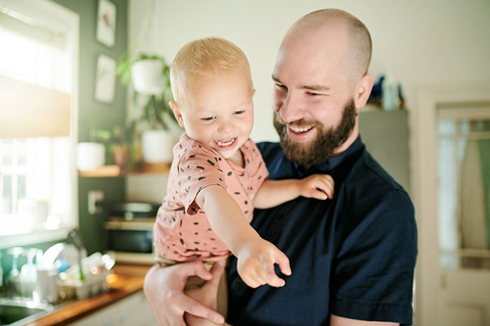 Father holding toddler in a bright kitchen, both smiling and enjoying a joyful moment together with kids.