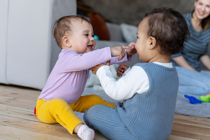 Two toddlers playing on a wooden floor while a woman watches, illustrating reasons people give to have kids.