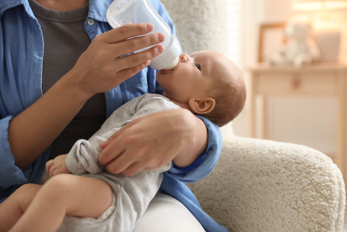 Woman feeding baby with bottle indoors, illustrating reasons people give to have kids and parenting moments.