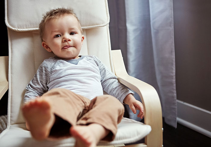 Toddler sitting in a white armchair at home, capturing a candid moment related to reasons people give to have kids.