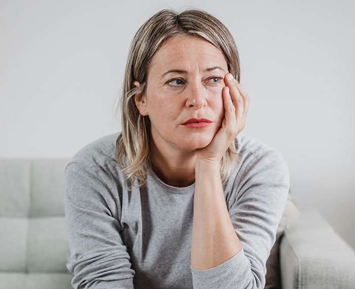 Woman in a gray shirt sitting thoughtfully on a couch, reflecting on reasons people give to have kids.