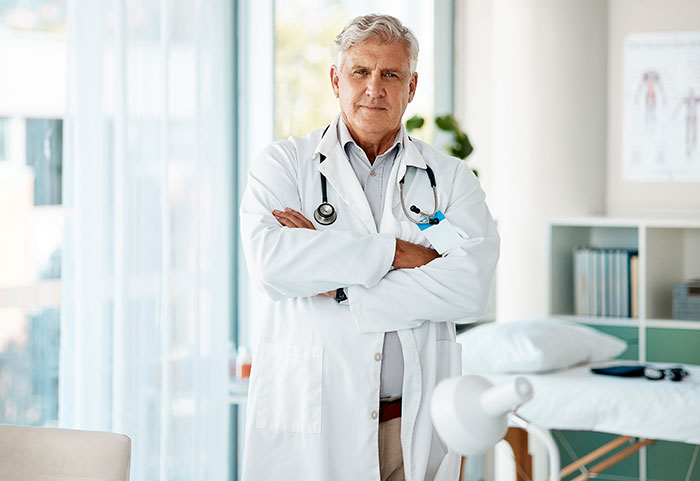 Middle-aged male doctor standing in a bright medical office with a stethoscope, representing reasons people give to have kids.