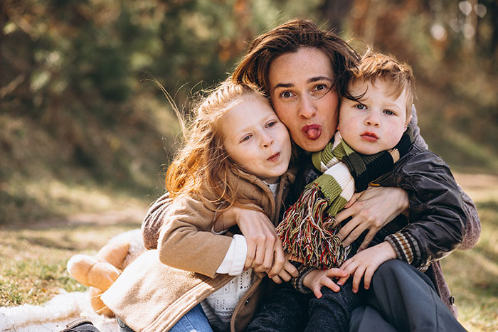 Mother hugging her two young children outdoors, capturing a playful moment about reasons people give to have kids.