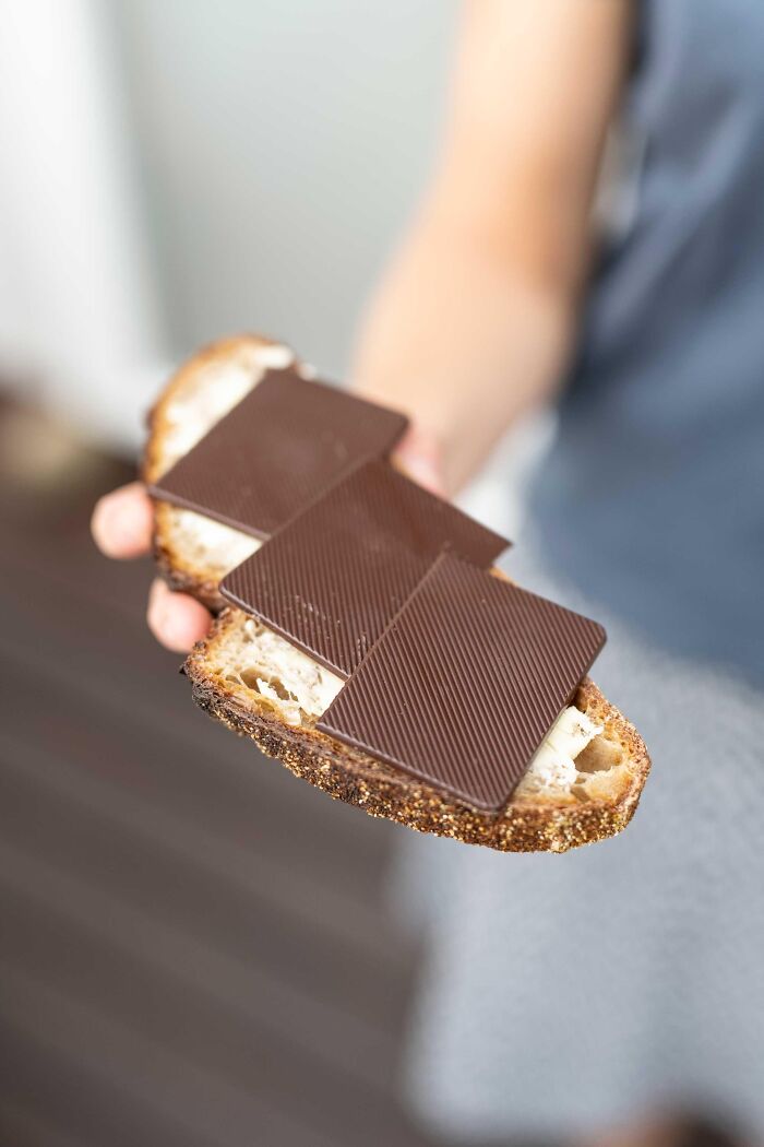 Person holding a slice of bread topped with butter and three large pieces of chocolate showing unique food habits worldwide.