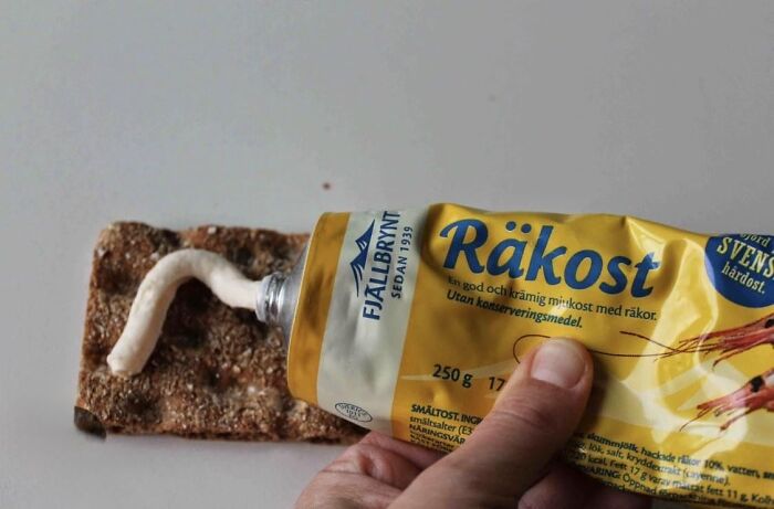 Hand squeezing Swedish räkost cheese spread from a tube onto crispbread, a common food in some countries.