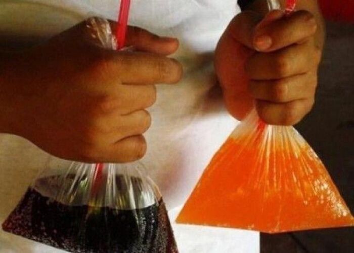 Person holding two plastic bags filled with soft drinks, showcasing common cultural practices in different countries.