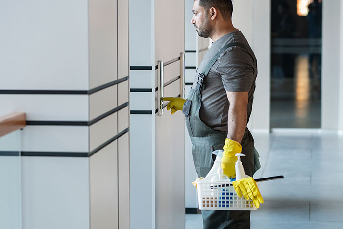 Man wearing yellow gloves and gray overalls holding cleaning supplies, representing lives of ultra-popular guys in adulthood.