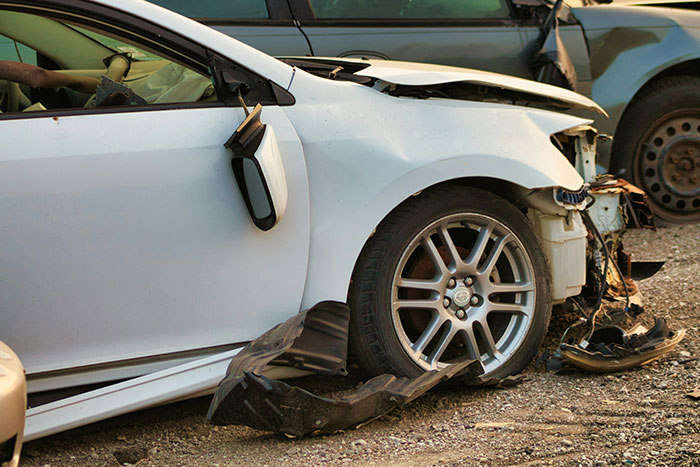 Damaged white car with detached bumper and broken side mirror, illustrating challenges in the lives of ultra-popular guys.
