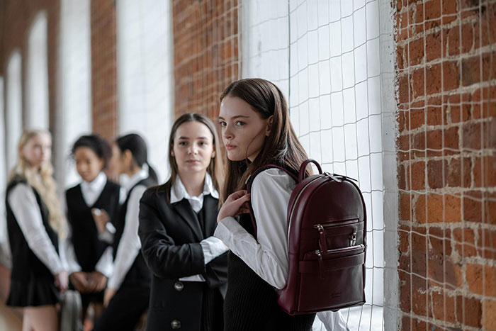 Teen girls in school uniforms standing against a brick wall, illustrating social dynamics of ultra-popular guys in adulthood.