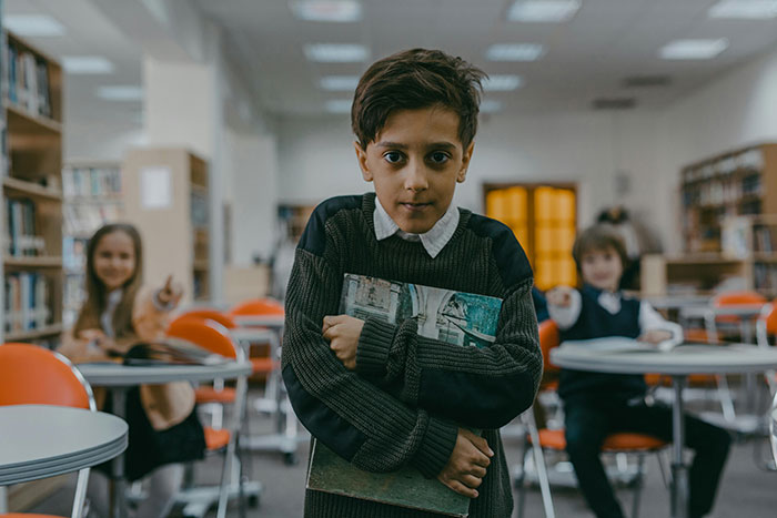 Boy in a sweater holding a book in a classroom, representing how lives of ultra-popular guys unfolded in adulthood.