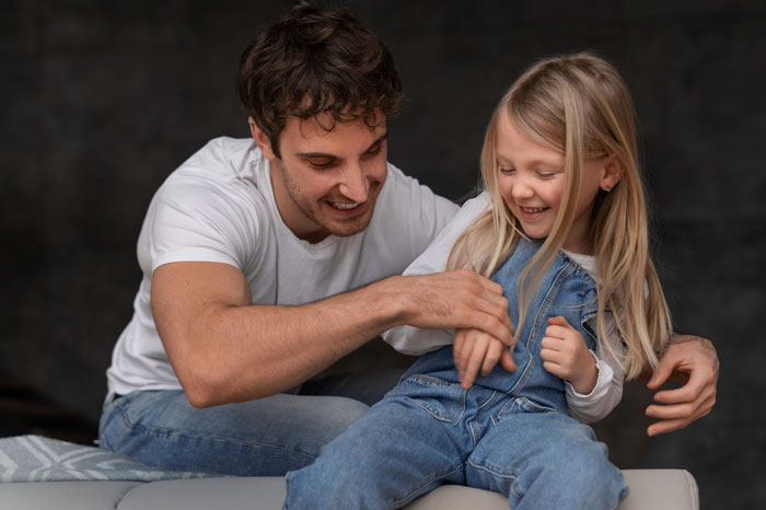Man playing and smiling with underage girl in denim overalls, reflecting wife refuse adopt underage sister situation.