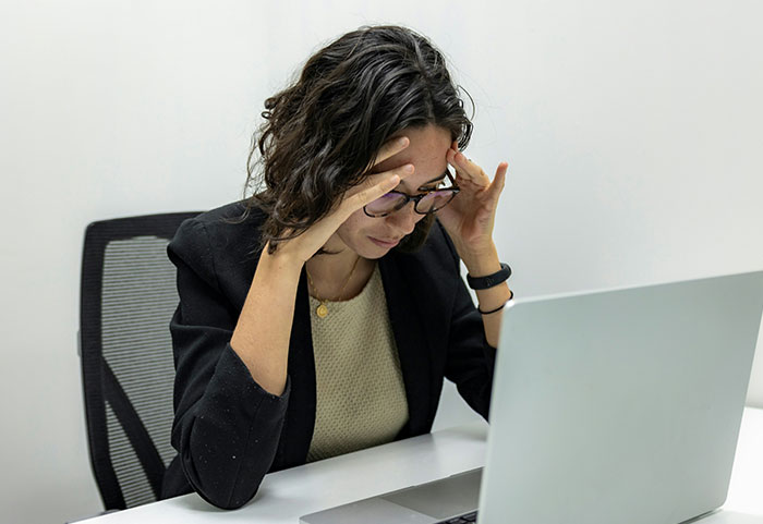Frustrated woman at laptop holding head, illustrating unhinged workplace incidents and stressful job situations.