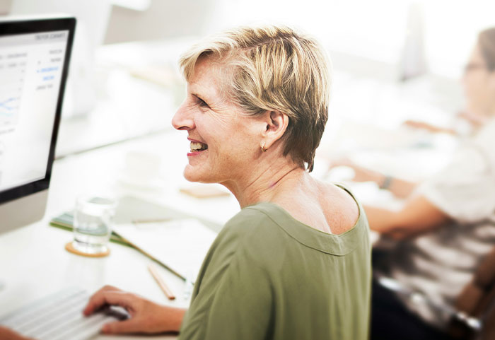 Smiling woman working at computer in office setting illustrating unhinged workplace incidents and job challenges.
