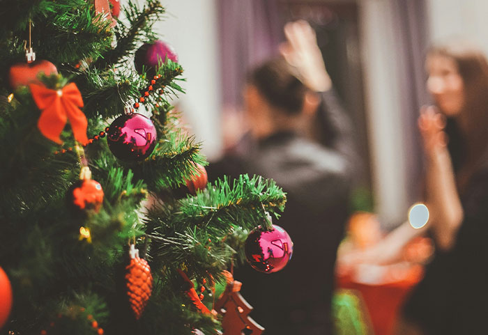 Close-up of Christmas tree decorations with blurred coworkers in background, illustrating unhinged workplace incidents.