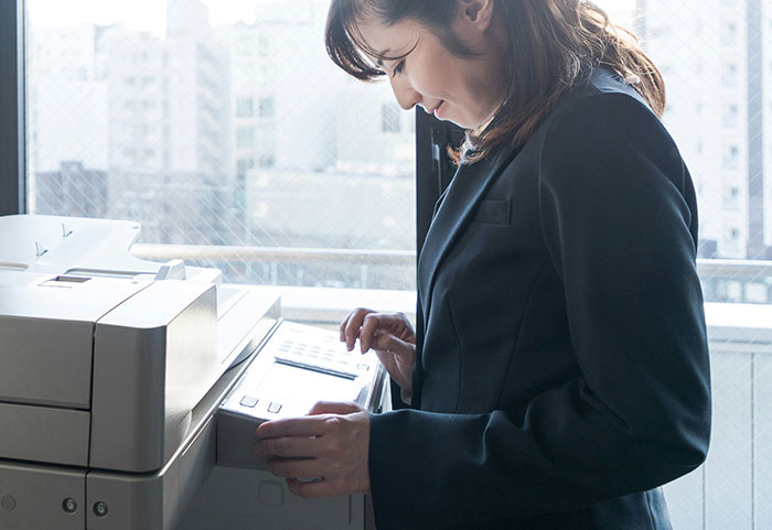 Woman in a black blazer using a photocopier in an office, illustrating unhinged workplace incidents and job realities.