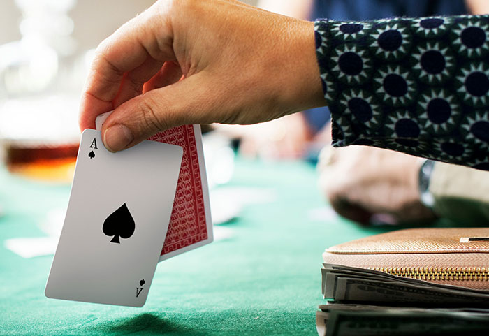 Hand holding an ace of spades card during a workplace game, illustrating unhinged workplace incidents and job stress relief.