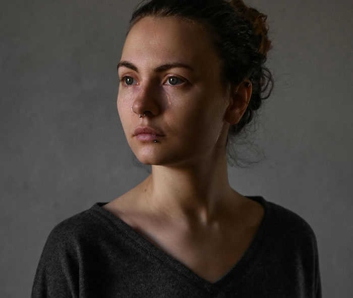 Young woman with teary eyes and neutral expression telling drunk boyfriend to stop acting like a jerk in low light.