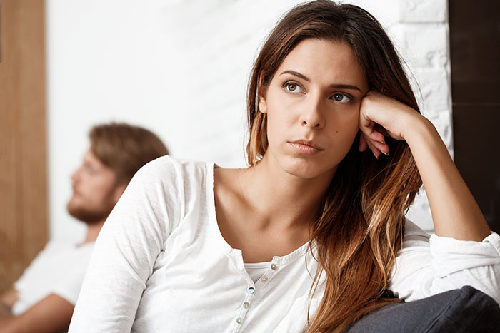Young woman with a pensive expression sitting on a couch, showing frustration in a fun sock collection dispute with boyfriend.