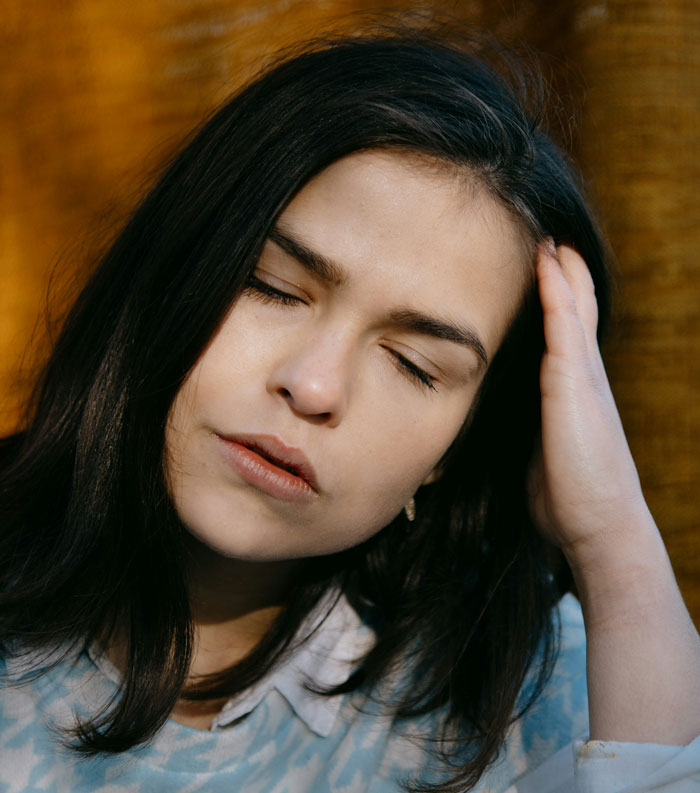 Woman with closed eyes, looking fed up and stressed, holding her head in frustration indoors.