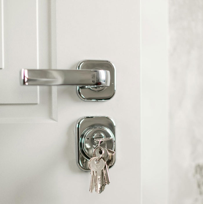 Close-up of a door handle with keys in the lock, symbolizing a woman fed up with being her roommates&rsquo; personal doorman.