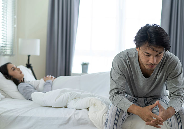 Couple in bedroom showing emotional distance after years of polyamory, reflecting on relationship struggles and personal feelings.