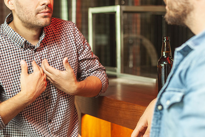 Two men in a bar having a serious conversation about an open relationship suggestion and breakup emotions.