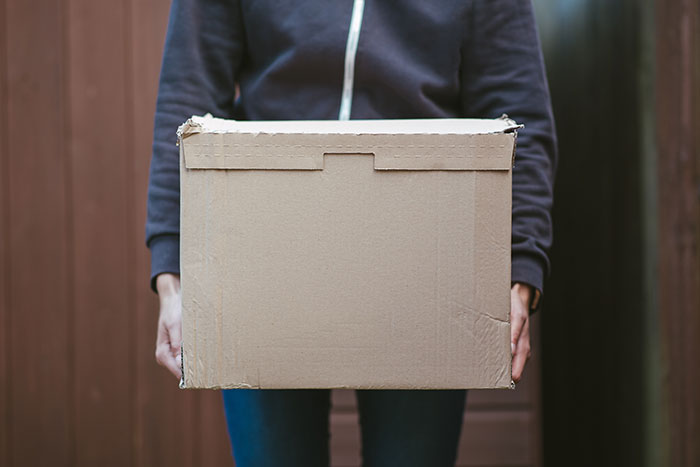 Person in casual clothes holding a cardboard box, symbolizing breakup and open relationship discussion.