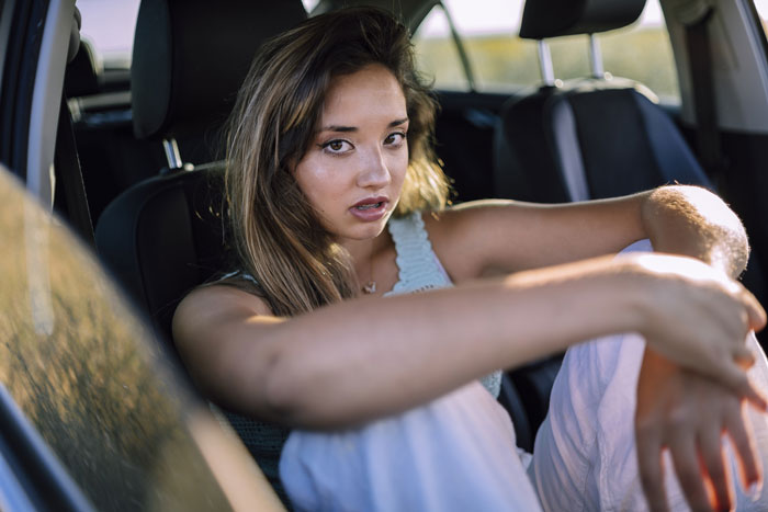 Woman sitting in a car looking thoughtful, reflecting on her party relationship with a partner during daylight hours.