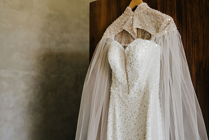 White beaded wedding dress hanging on a wooden door, related to attention-seeking mom dressing daughter like bride.