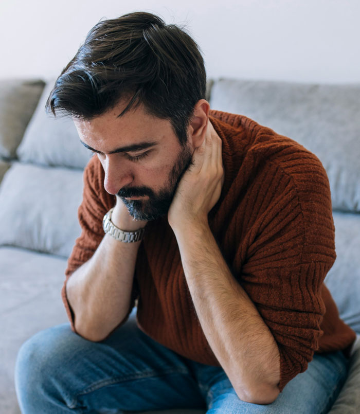 Man looking stressed sitting on couch, reflecting on his girlfriend refusing to wear dresses for a wedding.