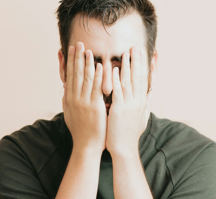 Man covering his face with hands showing frustration over girlfriend refusing to wear dresses for a wedding event